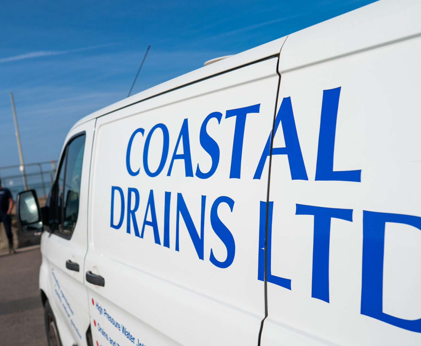 A man in safety glasses and gloves operates a red machine with gauges and hoses. Sunlight casts shadows, conveying a focused and industrious tone.